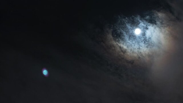 timelapse con vista dettagliata di un cielo notturno, parzialmente sereno e con qualche nuvola, che mostra la rotazione terrestre, le stelle e il movimento della luna piena