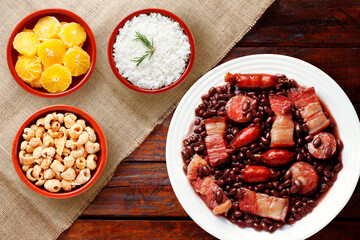 A plate of traditional Brazilian feijoada with meats, sausages, rice, orange, and pork crackling served on a rustic wooden table