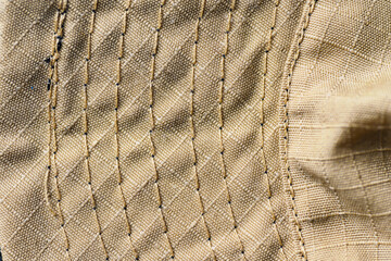 Macro view of tan ripstop textile showing detailed weave and multiple parallel rows of heavy-duty reinforced stitching, ideal for tactical, military, or industrial fabric backgrounds