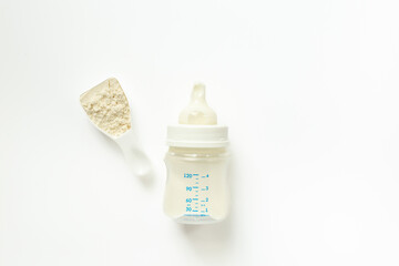 Powdered infant formula in a scoop and baby milk bottle on white background. Top view.