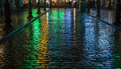 Obraz premium Wet Cobblestone Street at Night with Green Light Reflections