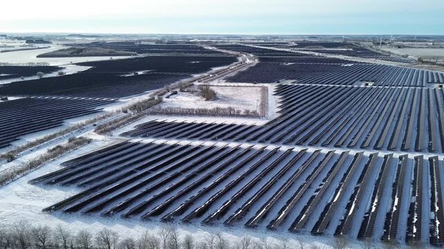 Aerial video of a large solar park in Denmark during winter, with snow-covered ground and parallel panel rows.