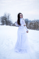 Snow Queen. A young girl in a white dress in the snow. Girl in a white dress. Bride. Winter cold weather. Model. Young woman in winter park.