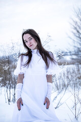 Snow Queen. A young girl in a white dress in the snow. Girl in a white dress. Bride. Winter cold weather. Model. Young woman in winter park.