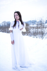 Snow Queen. A young girl in a white dress in the snow. Girl in a white dress. Bride. Winter cold weather. Model. Young woman in winter park.