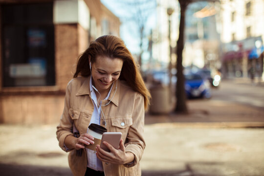 Smiling young woman with earphones using smartphone on city street