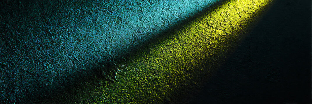 A textured wall illuminated by a narrow beam of contrasting light, revealing rich hues of blue and green, creating a dramatic interplay of color and shadow.