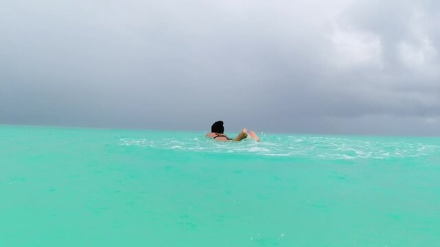 Pretty Woman swimming alone in calm turquoise indian ocean during tropical rain cloudy sky monsoon mood slow travel off-season concept