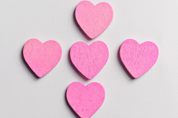 Fototapeta premium Five small pink wooden hearts arranged in a cross pattern on a white textured background. A minimal and romantic composition perfect for Valentine's Day, love, and greeting card designs