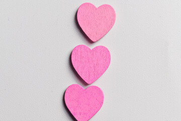 Fototapeta premium A vertical arrangement of three small, bright pink wooden heart shapes centered on a textured white surface, perfect for Valentine's Day or romantic themes