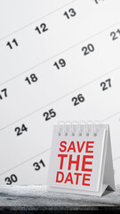 Desk flip calendar with Save the Date in red text on a stone surface with a blurred calendar background. Ideal for wedding, party, or business meeting reminders and event planning