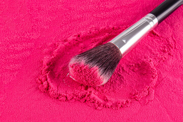 A fluffy professional makeup brush rests on a bright pink background of loose blush. Front view. Decorative cosmetics concept.