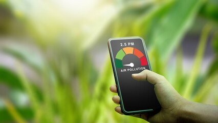 A person checks high air pollution levels and PM2.5 on a mobile app while outdoors. The digital gauge shows poor air quality against a blurred green plant background
