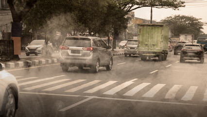 Busy urban traffic with cars and a truck driving through thick air pollution and smog on a city road. Represents environmental issues, climate change, and health risks in cities