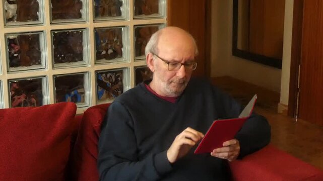 Older man with glasses using tablet on sofa