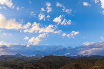 Expansive mountainous landscape features rolling hills and distant peaks under a cloudy sky. Late afternoon light casts a serene glow over the natural scenery.