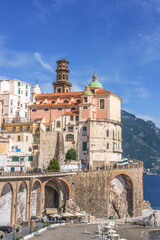 Obraz premium Amalfi Coast, Italy, Atrani,. Coastal village with colorful buildings and a historic church perched on a cliff overlooking the sea under a clear blue sky with mountains in the background