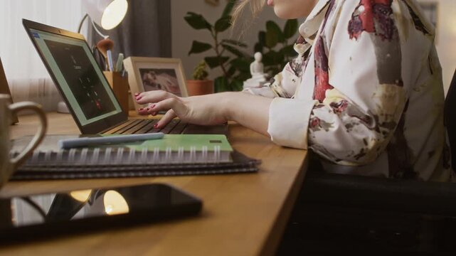 Tilt up midsection shot of girl with disability typing on laptop at wooden table while sitting in wheelchair at home