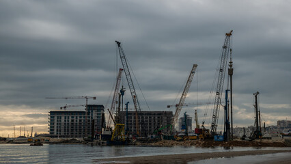 Fototapeta premium Building construction on the coast with cranes, new development near the sea.