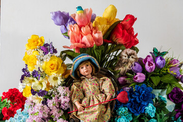 young girl doll with glass eyes sitting in front of spring flowers holding red heart