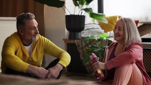 Happy couple in their 50s sitting on yoga mats and discussing recent training