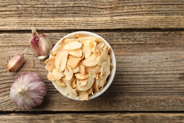 Dried garlic flakes in bowl and fresh vegetables on wooden table, flat lay. Space for text