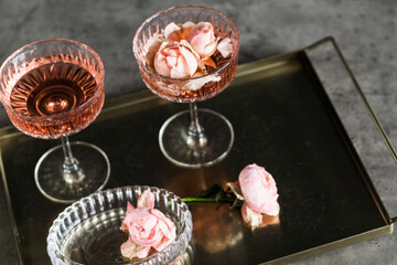 Elegant glassware with pink rose petals and sparkling rose wine on a metallic tray, showcasing a...