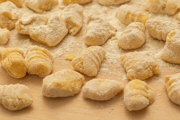 Close-up of fresh homemade gnocchi dusted with flour on wooden board, ideal for Italian cuisine branding, recipe blogs, cooking tutorials, and rustic food visuals