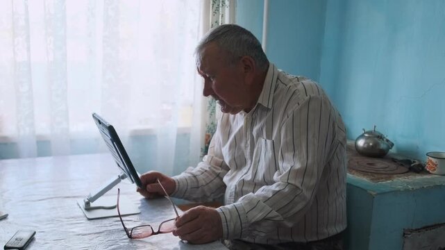 Senior Reads Attentively - Old Man Uses Tablet Carefully - Elderly Gentleman With Glasses Concentrates On Reading - An Aged Gentleman Wearing Glasses Attentively Focusing On Digital Reading In Soft