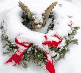 A garden gargoyle in the middle of a Christmas wreath in the snow.