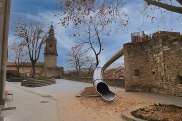 Modern Slide in Historic Town Square Park; Large metal playground slide contrasting with ancient...