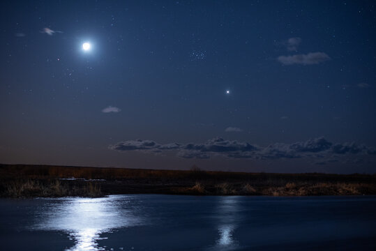 Bright moon and star over calm river at night.
