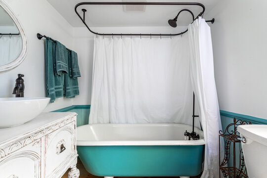 Vintage style bathroom interior with turquoise clawfoot bathtub, white shower curtain and rustic vanity