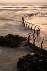 Fototapeta premium A rocky coastline with a metal fence and a pier at La Punta del Hidalgo in Tenerife, Canary Islands. The water is choppy and the sky is cloudy