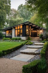 Modern house with large windows surrounded by green trees and well-kept garden path leading to the entrance in the late afternoon light