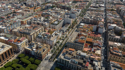 Wide aerial view of a historic city center. Densely packed buildings with classic architecture are intersected by a long, straight main road. It is located in Messina, Sicily, Southern Italy.