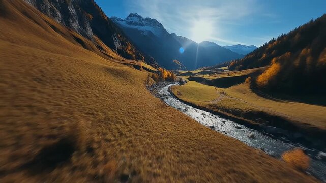 Stunning aerial view of a sunlit alpine valley during autumn with a winding river.