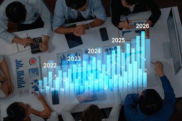 A business team collaborates over data analysis featuring charts and graphs, highlighting growth trends and future projections from 2023 to 2026. Trope