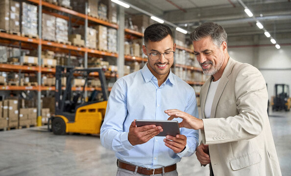 Team of two happy professional warehouse managers working standing in storage using digital tablet. Logistic commercial retail goods supply. Storehouse distribution, industrial merchandise, delivery.