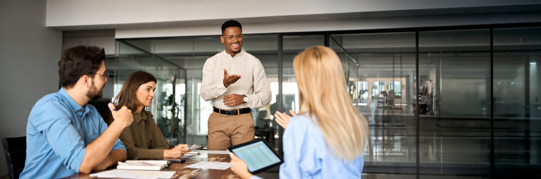 Young happy African American male executive company leader discussing project management planning strategy working with diverse busy colleagues company team at office corporate board group meeting.