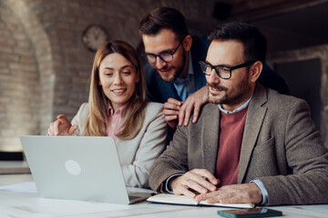 Professional business team working together on a laptop in a modern office, discussing project details and analyzing digital data.

