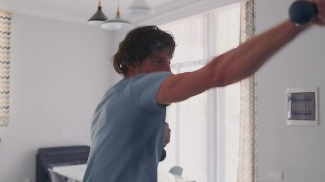 caucasian man shadowboxing with dumbbells kitchen living area, determined punches, quick footwork, blue shorts, gray tshirt, bright window light, modern minimal kitchen, fruit bowl on table,