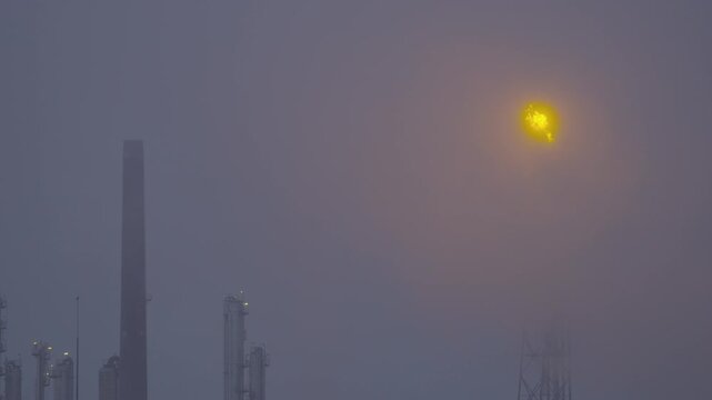 Industrial chimney flaring off excess gas in fog.
