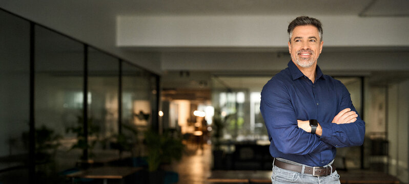Happy mature 50 years old professional banker business owner man manager, smiling senior male ceo executive, middle aged corporate leader looking away standing arms crossed in office at work.