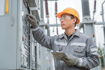 Technician inspecting electrical substation equipment with tablet in hand