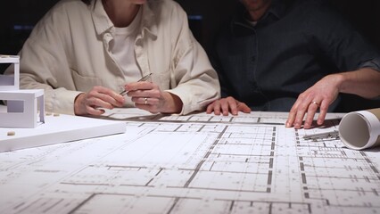 Architects and engineers collaborating on a new building project, planning structural details and design concepts using blueprints and a scaled architectural model on a desktop