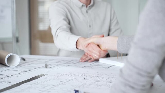 Handshaking between two architects finalizing a construction project deal, business partners agreeing on engineering blueprints and architectural models in an office, close up