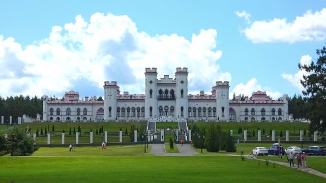 Visitors walk around The Puslovsky Palace in Kossovo  a large castle surrounded by gardens and trees. People enjoy the area's beauty while sitting on benches and walking along paths.