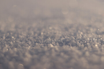 Snowy background with selective focus. The surface is covered with snow, snowflakes sparkling in the sun. The snowy surface shines in the sun, blurred background. Winter background. Cold season