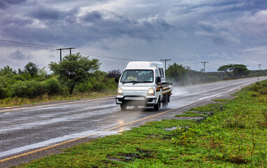 White light commercial truck with a flatbed drives on a rain-slicked highway during a storm